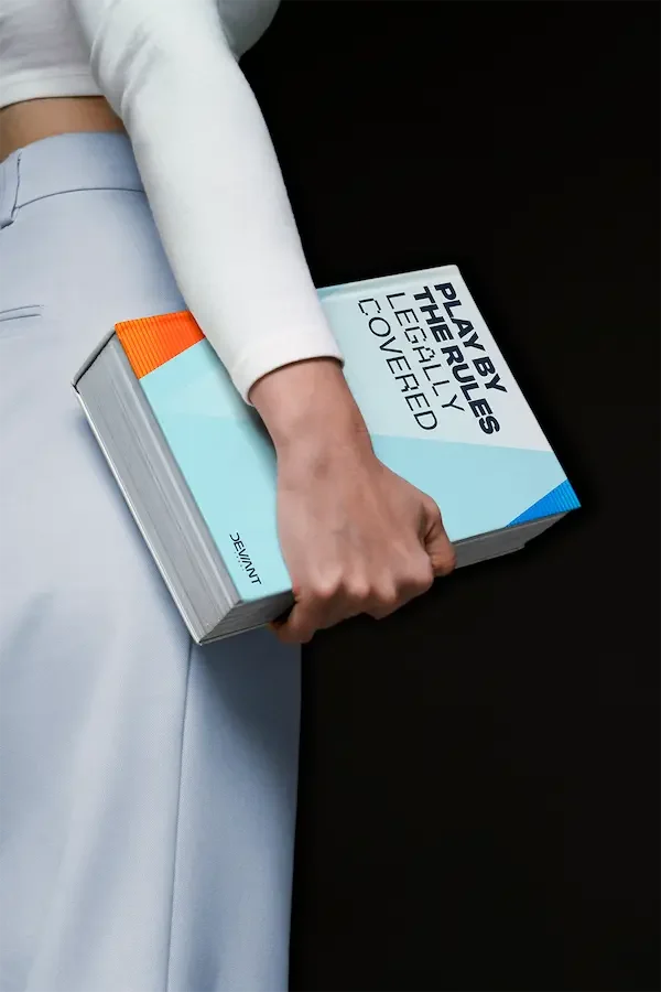 Person holding a thick book with the title “Play by the Rules. Legally Covered.”