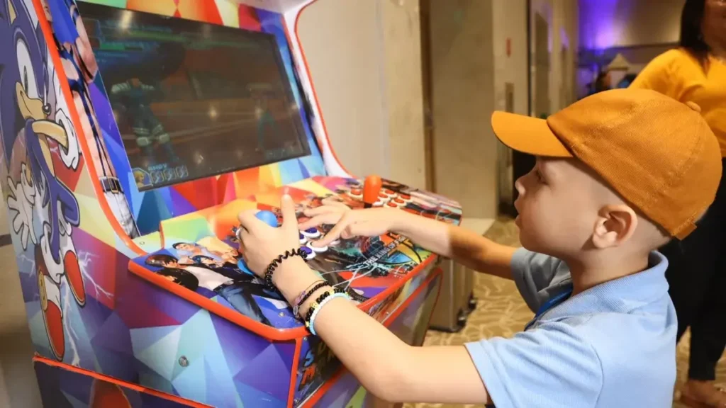 Child playing an arcade game, smiling and focused at the controls.