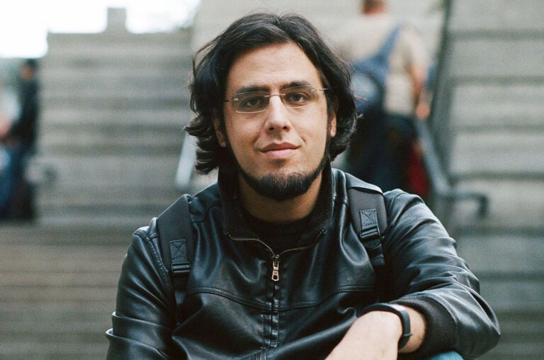 Rami Ismail, seated outdoors and facing the camera with a slight smile.